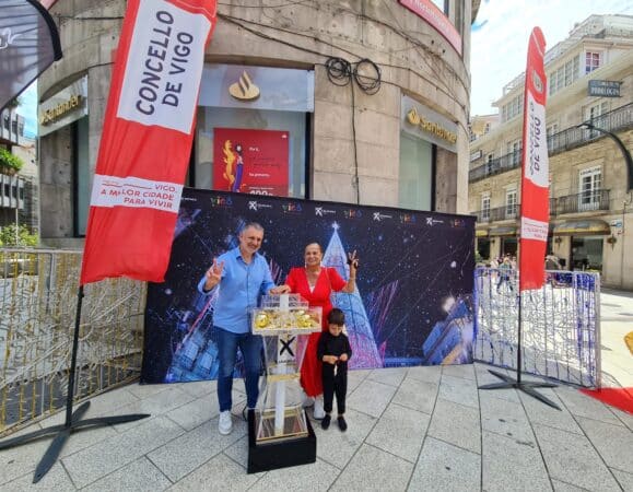 Tres personas posan frente al edificio del Taller de las Luces de Navidad de Vigo, donde se observa un gran cartel navideño